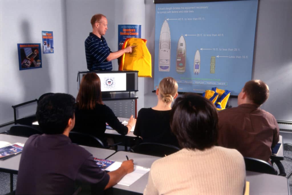 A man holding up a life jacket in front of a classroom.